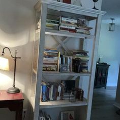 a book shelf with books on it in a living room next to a table and lamp