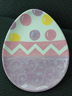 an egg shaped plate painted with pink, yellow and purple polka dots on green fabric