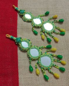 two green and yellow beaded mirrors sitting on top of a red cloth covered table