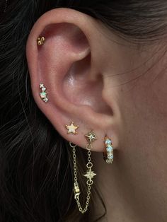 a woman's ear is adorned with three stars and two danglings, all in gold