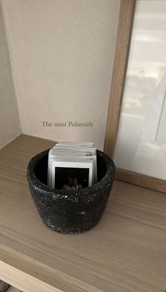 there is a small black bowl on the table with magazines in it and a mirror behind it