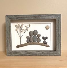 a shadow frame with rocks and flowers in it on a wooden table next to a wall