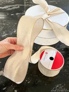 a hand holding a ribbon next to a white box with a red stripe on it