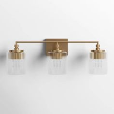 three light brass bathroom fixture with clear glass shades on the sides and gold fixtures, against a white wall