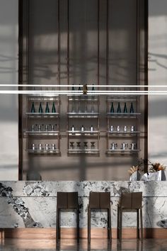 three chairs sitting in front of a marble counter with bottles on the wall behind them