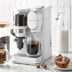 a white coffee maker sitting on top of a counter next to a plate of food