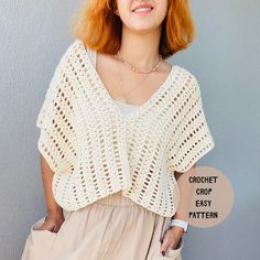 a woman with red hair wearing a crochet crop top and beige skirt is smiling at the camera