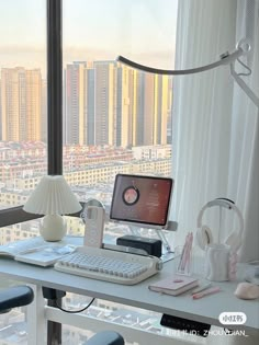 a desk with a computer and headphones on it in front of a large window