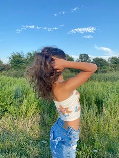 a woman standing in the grass with her hands behind her head and looking into the distance