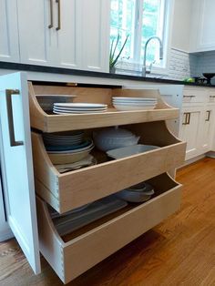 an open drawer in the middle of a kitchen with plates and bowls stacked on it