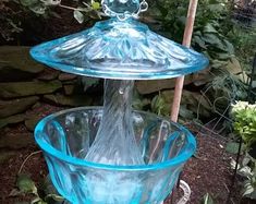 two blue glass bowls sitting next to each other on top of a garden stand in front of flowers