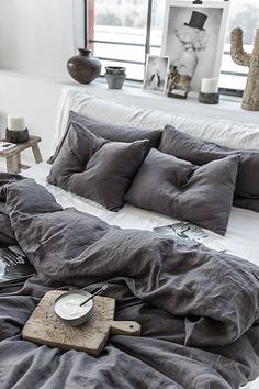 an unmade bed with grey linens and pillows