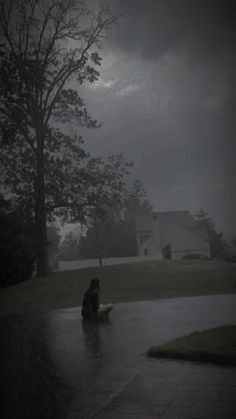 a person sitting on the ground in the rain with an umbrella over their head,