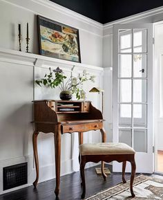 a room with a chair, desk and painting hanging on the wall above it's doorway