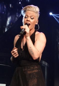 a woman in a black dress holding a microphone and singing into the air at a concert