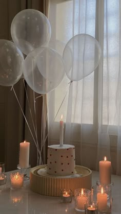 a table topped with lots of white balloons next to candles and a cake covered in frosting