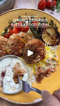 a yellow plate topped with meat and veggies next to a bowl of sauce