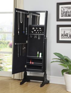 a black jewelry cabinet sitting on top of a wooden floor next to a potted plant