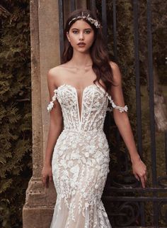 a woman in a wedding dress standing next to a iron gate and posing for the camera