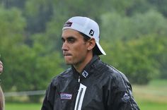 a man wearing a white hat and black jacket standing next to another man in the rain