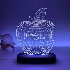 an illuminated apple with the words delicious on it and a small white object in the background