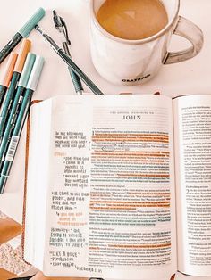 an open bible with markers and pens next to it on a table near a cup of coffee