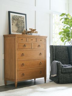 a wooden dresser sitting next to a gray chair in a living room with white walls