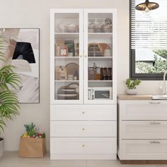 a white cabinet with glass doors and drawers in a kitchen next to a potted plant