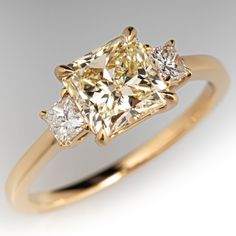 three stone diamond ring with yellow gold and white diamonds on the sides, set against a plain background