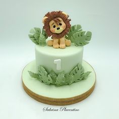 a cake with a lion on top and green leaves around the edges, sitting on a plate