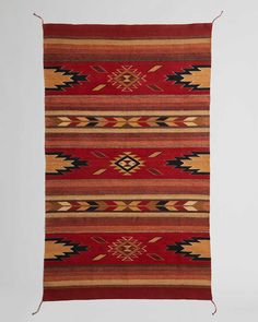 a red, yellow and black navajo rug hanging on a wall with white walls in the background