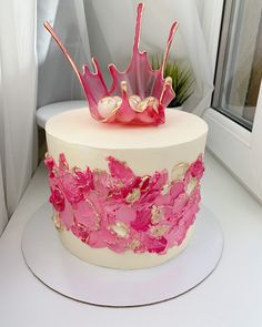 a white and pink cake with flowers on the top is sitting in front of a window