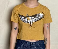 Our hand-drawn Red-Tailed Hawk design is printed in brown, white and orange on this super soft, raw-edge gold tee.   Available in  XS -2XL.  Runs a little small, order up for a slouchier fit. One model is an XS and wearing an XS. Other model is a medium/ large and wearing a large.  See size chart and message me with any questions.  Soft, lightweight 65%Poly/35%Cotton, sweatshop free. Our original, hand-drawn designs are printed on sweat-shop free clothing using environmentally conscious water-ba Mustard Short Sleeve T-shirt With Graphic Print, Hand Printed Crew Neck Graphic Tee, Hand Printed Graphic Tee With Crew Neck, Hand Printed Short Sleeve Graphic Tee, Casual Crew Neck Hand Printed T-shirt, Casual Hand Printed Crew Neck T-shirt, Hand Printed Crew Neck Top With Relaxed Fit, Relaxed Fit Hand Printed Crew Neck Top, Vintage Hand Printed Crew Neck Tops