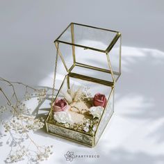 a glass box filled with flowers and baby's breath on top of a white surface