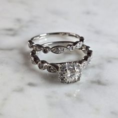 two wedding rings sitting on top of a marble countertop, with one diamond set in the middle