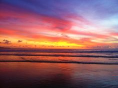 the sun is setting over the ocean with clouds in the sky and water on the beach