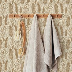 two towels hanging on a towel rack in front of a wallpapered wall with leaves