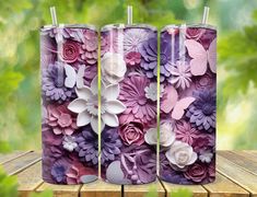 three tumbles with flowers painted on them sitting on a wooden table in front of green leaves