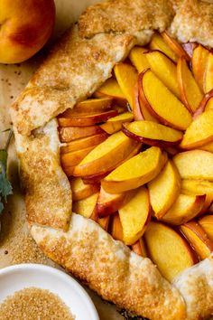 a pie with sliced peaches on it next to two small bowls and a leaf