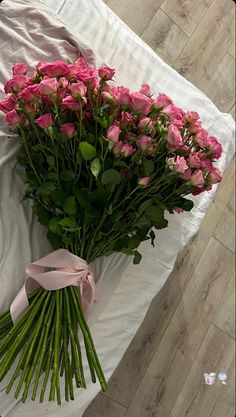 a bouquet of pink roses sitting on top of a white bed sheet next to a pillow