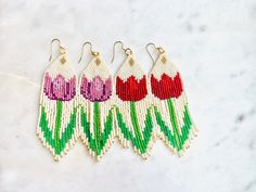 three pairs of beaded earrings with tulips hanging from them on a marble surface