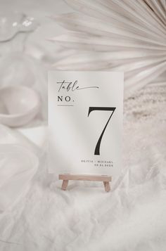 a white table number sitting on top of a wooden stand next to plates and bowls