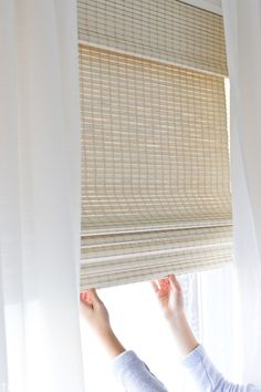 a woman is looking out the window with her hand on the blinds that are closed