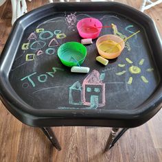 a black tray with chalk writing on it and two buckets filled with colored paint