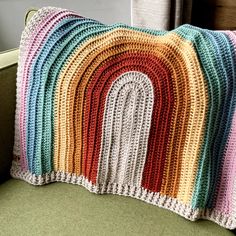 a multicolored crocheted pillow sitting on top of a green couch next to a window