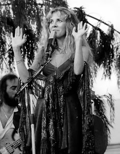 a black and white photo of a woman singing into a microphone with her hands in the air