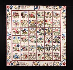 a square quilt with flowers and birds on the border is hanging in front of a black background