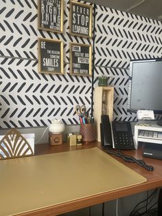 a desk with a computer, phone and other office supplies on it in front of a black and white wall