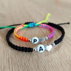 two bracelets with letters and hearts are sitting on a wooden table, one has the word pa written on it