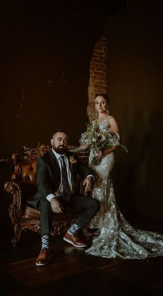 a bride and groom posing for a photo in front of a brick wall with an old chair